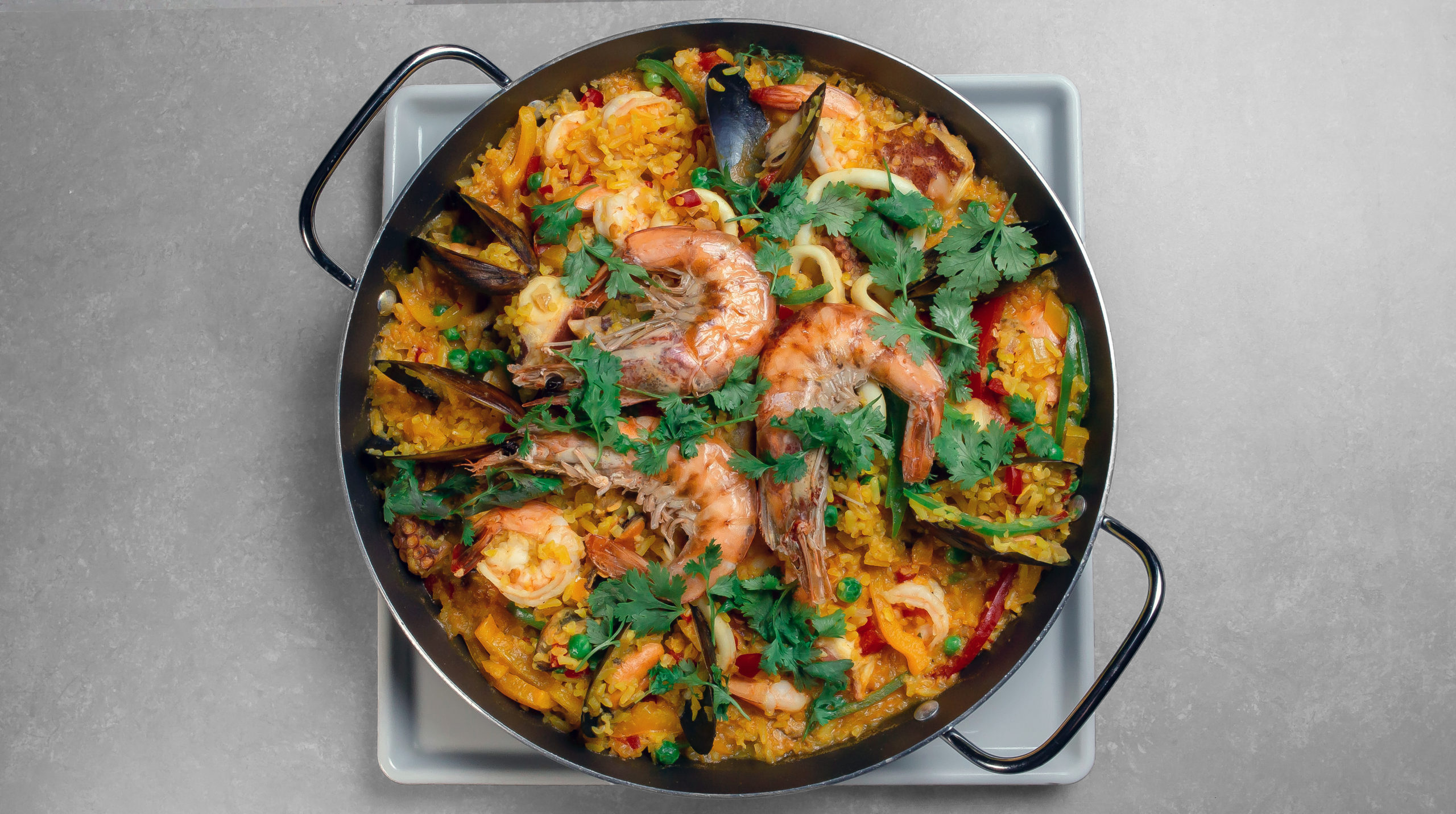 Seafood paella in a pan with shrimp, mussels, spanish rice, parsley and lemon on a plate.